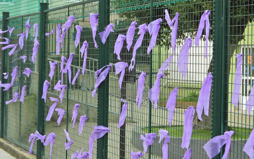 A photograph features numerous light-purple ribbons tied into bows across the surface of a large, green wire fence.