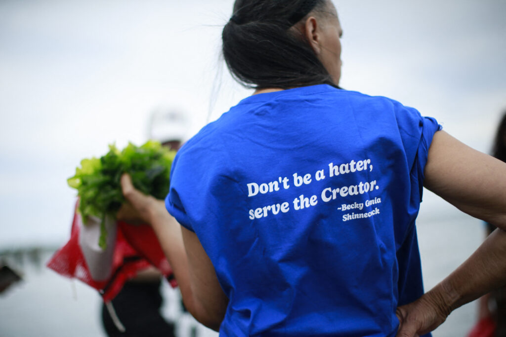 A person holding sugar kelp wears a blue T-shirt that reads: Don’t be a hater, serve the Creator.