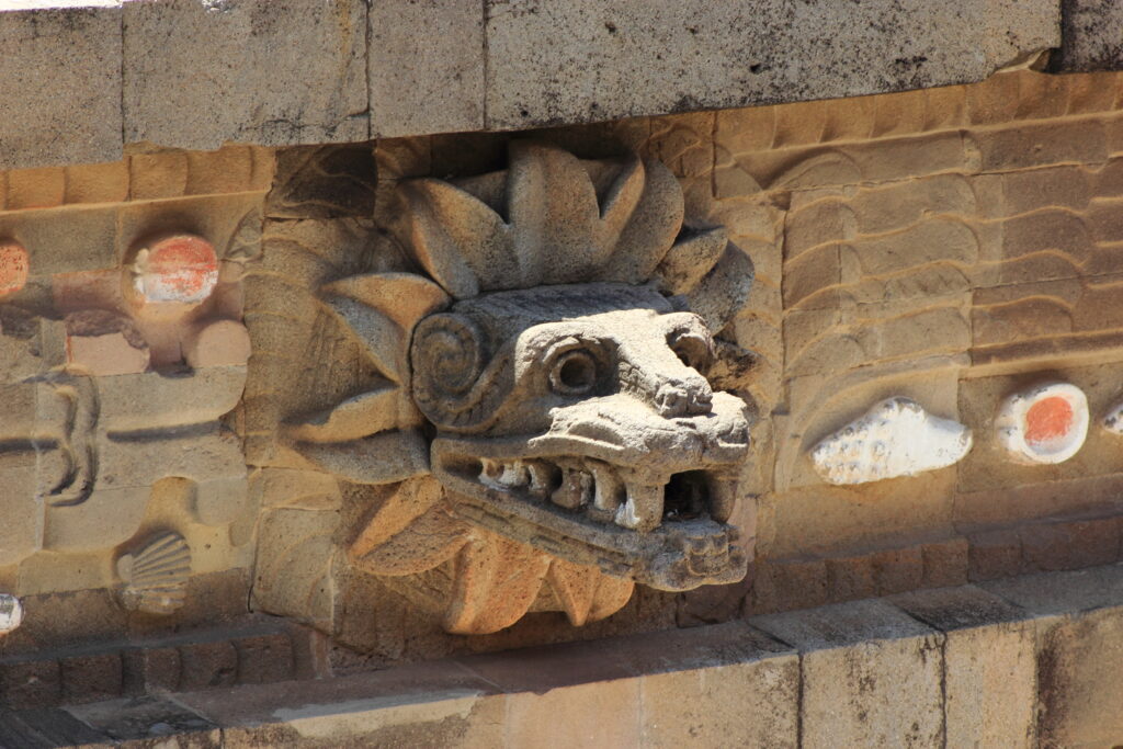 A stone carving on a wall resembles a snake head surrounded by feathers.