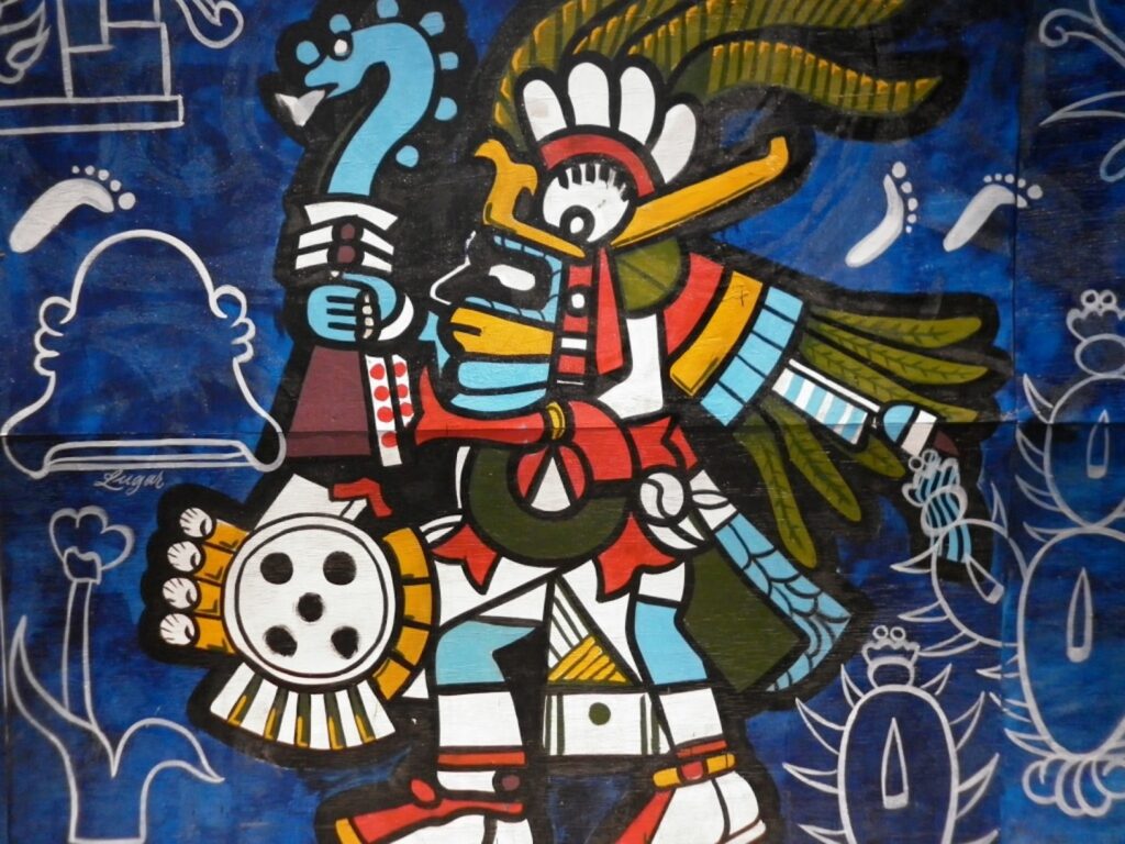 An illustration features a colorful semi-human figure with blue skin wearing a large feather headpiece and holding a blue serpent and a shield.