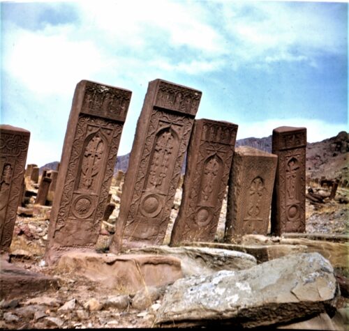 A photograph features several stone pillars, some tilting towards others, with etched angular and circular designs on their visible front side. Blue skies and mountains lie in the background.