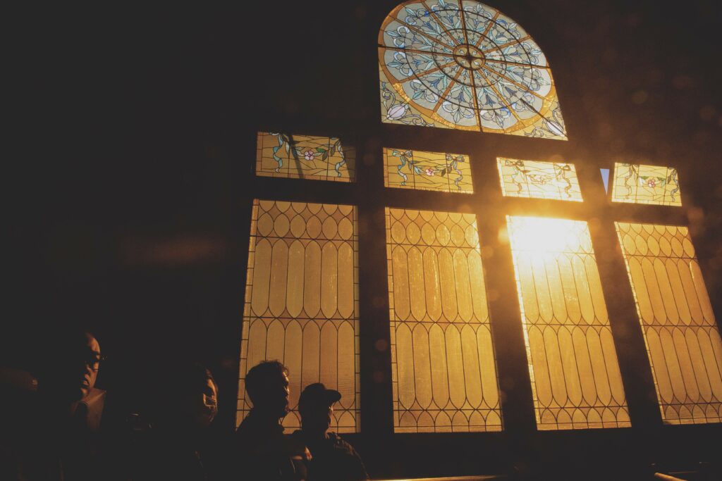 A photograph features the dark interior of a church backlit through a large stained-glass window. The silhouettes of several people fill the bottom left of the image.
