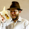 A man with a beard and hat holds an animal skull with antlers.