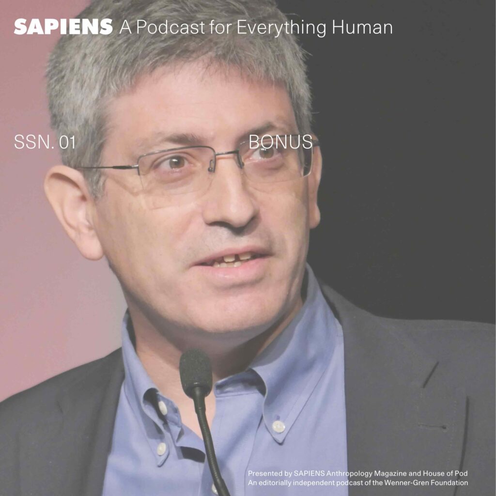 A middle aged white man in glasses is before a thin microphone speaking.