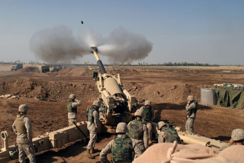 A battalion of soldiers gather around a cannon firing a missile that leaves a plume of smoke in its wake.