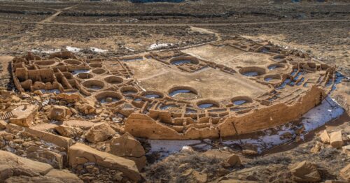 Una fotografía aérea muestra un gran complejo en forma de arco de ruinas de piedra que muestran los restos de habitaciones rectangulares y lugares de reunión sagrados circulares.