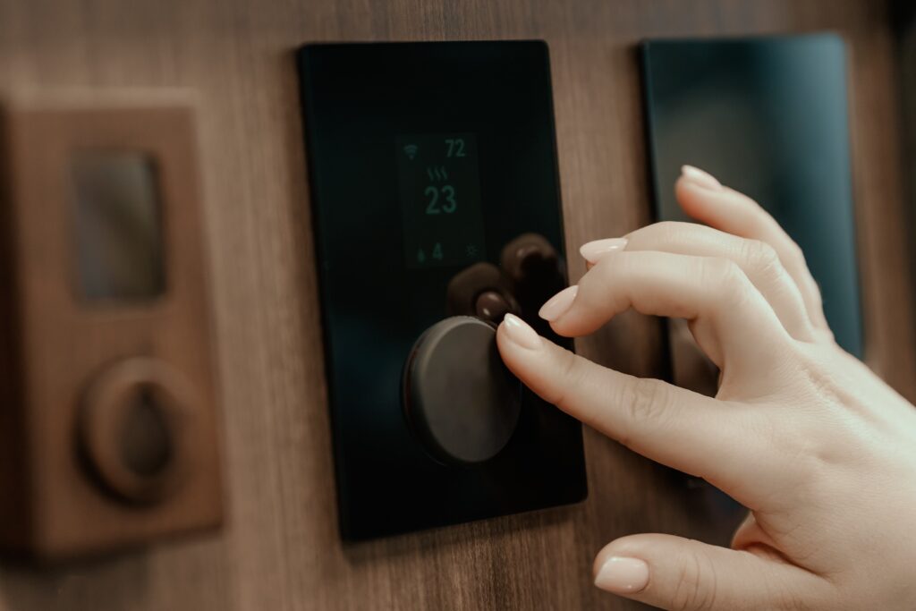 A close-up photograph features a person’s hand touching a temperature control module on a wood-paneled wall.