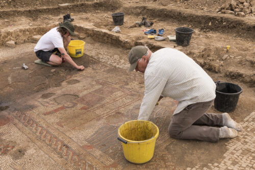 A photograph features two people kneeling by buckets and working to clean a tiled mosaic on the ground.