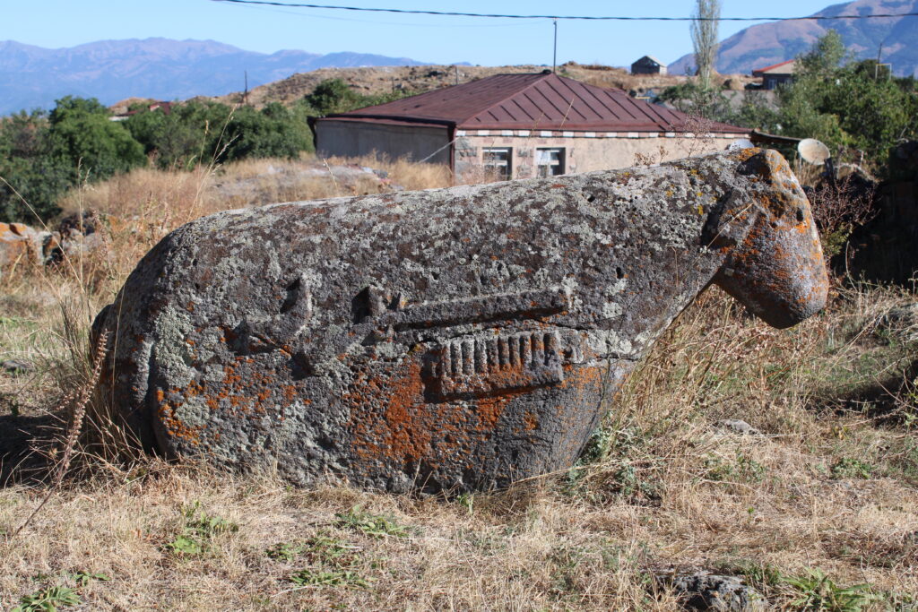 A gray sheep-shaped rock carved with weapons and equipment on its side stands in front of a beige stone building.