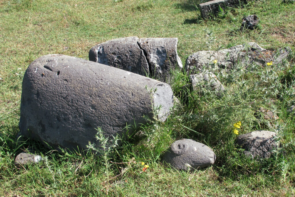 A sheep-shaped stone with its head knocked off stands in the grass in front of another broken sheep-shaped stone.