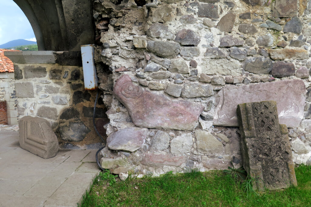 A building made of cobbled beige stones features a pink, sheep-shaped stone stuck into the wall.