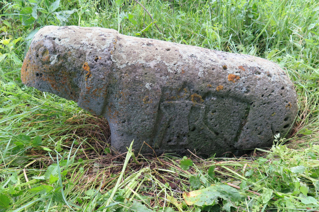 A gray sheep-shaped stone is etched with the figure of a man holding two long objects.