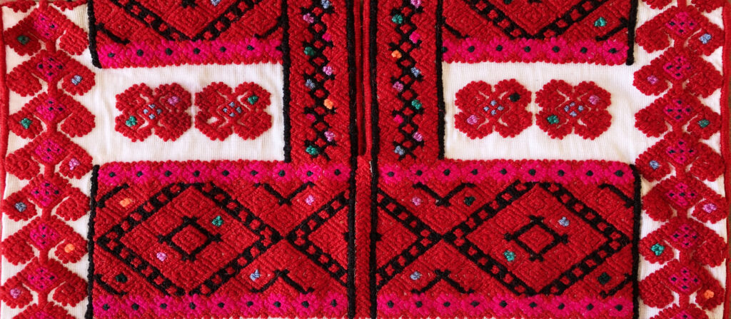 Un primer plano muestra una tela tejida en su mayor parte de color rojo, con dibujos diagonales que incorporan detalles en blanco, negro, verde y rosa fuerte.