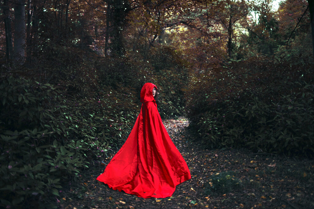 A photograph features a person in a red hooded cape standing in a dark forest, looking back at the viewer.