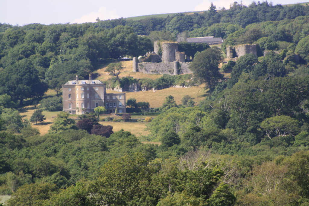 A photograph features a gray stone castle on a grassy hillside flanked by trees on all sides.