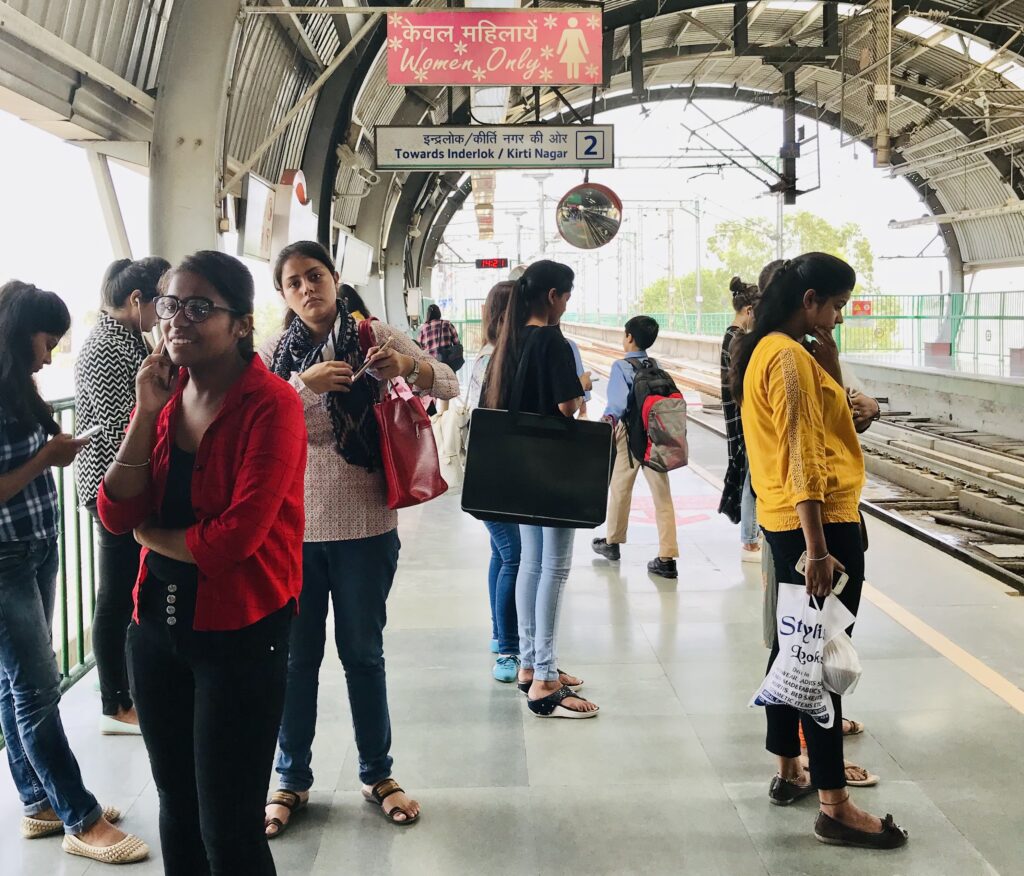 A photograph features several women standing on a metro platform, some facing other women and others facing the tracks.