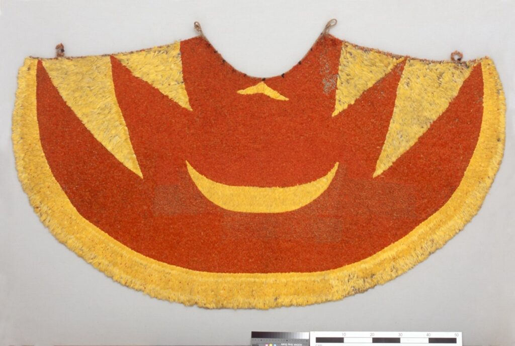 A large cloak featuring a dark orange and yellow pattern similar to flames hangs on a gray wall.