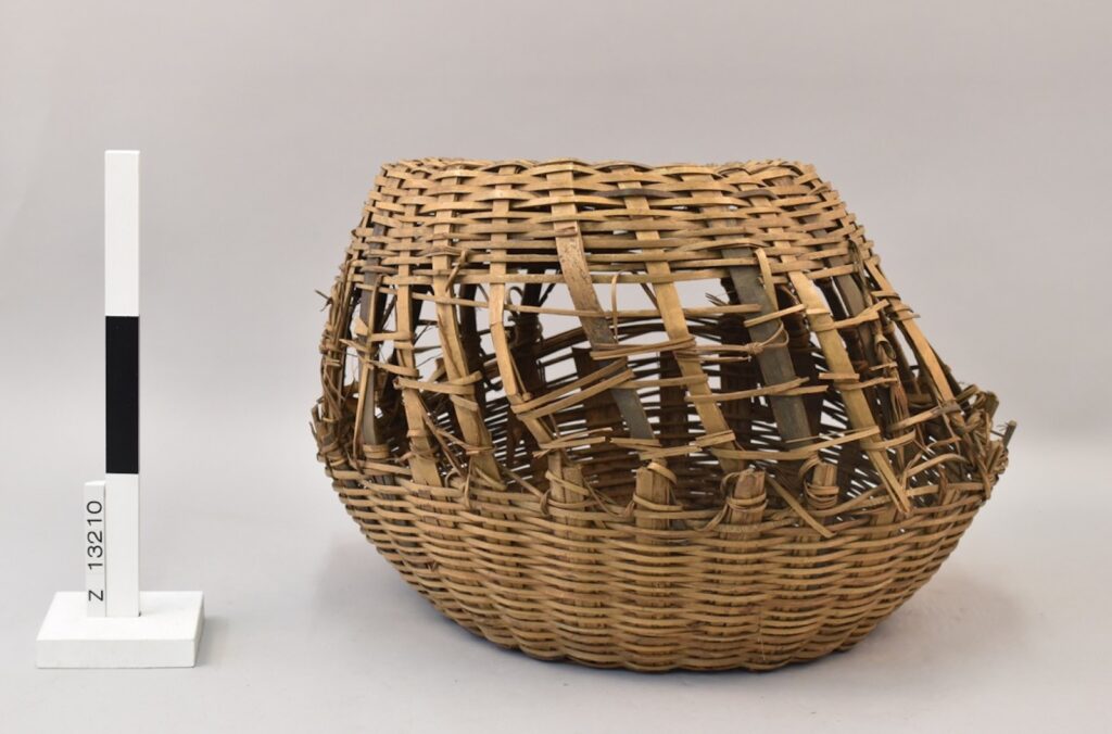 A photograph features a weathered straw basket next to a standing black-and-white measuring stick.