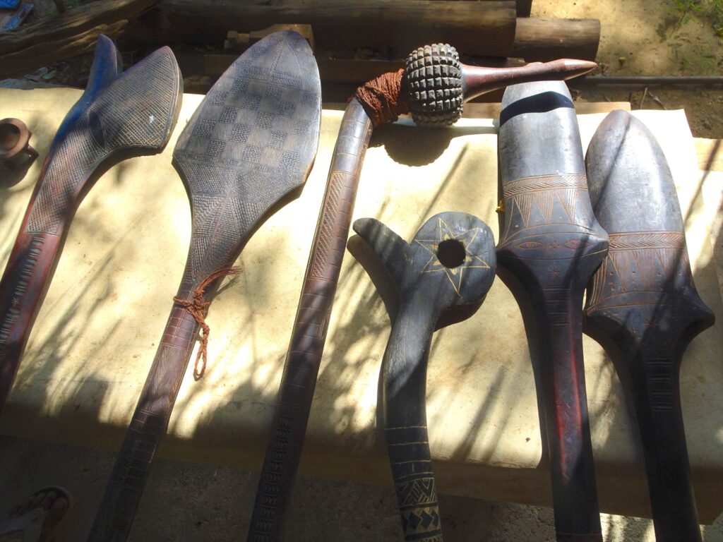 A photograph features six differently shaped and ornately carved wooden sticks on a cement table.
