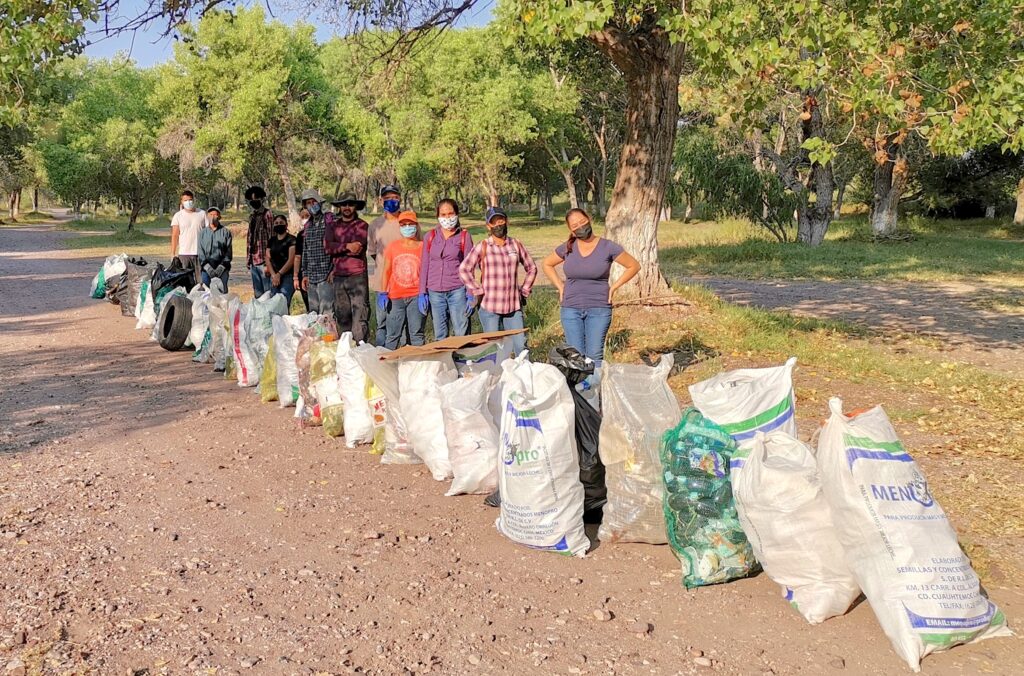 A photograph shows 12 masked people in a line standing next to a row of white trash bags and a few large pieces of debris.