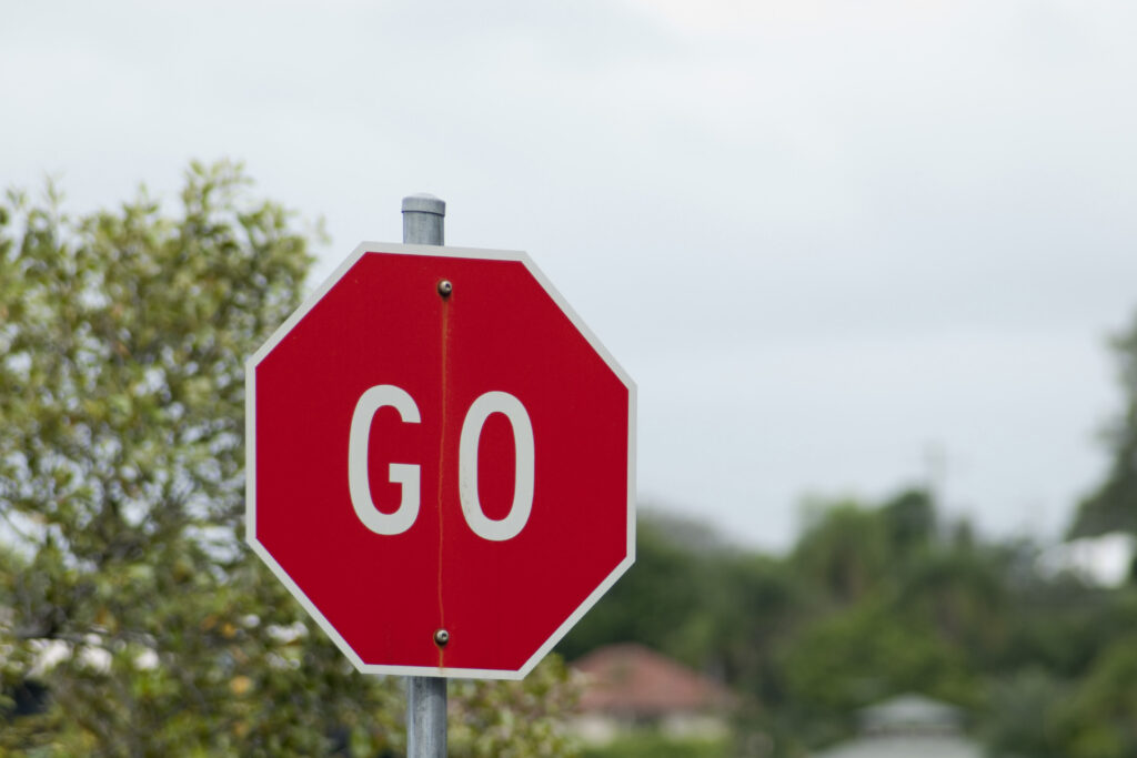 A red octagonal sign on a metal post has the word “GO” written on it in white.