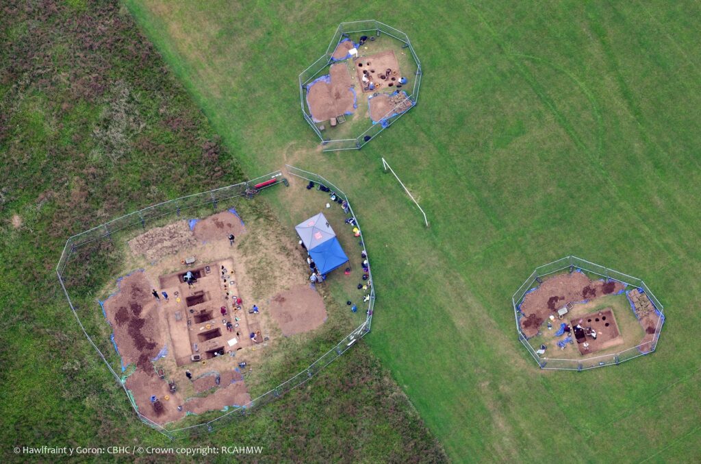 An aerial photograph shows three large areas of brown soil containing rectangular holes within a larger field of green grass.