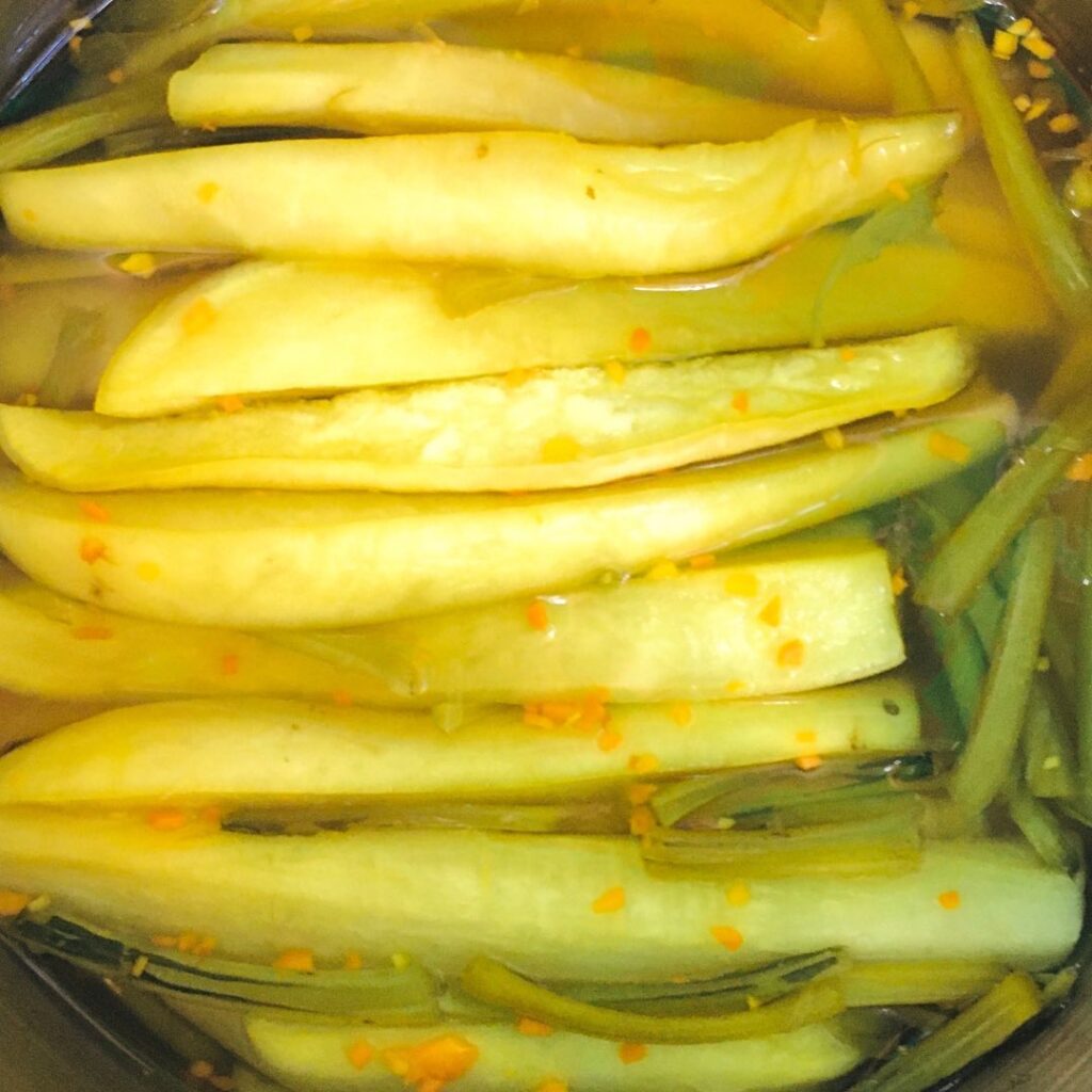 A close-up photograph features long sliced vegetables in a clear liquid covered in orange specks.
