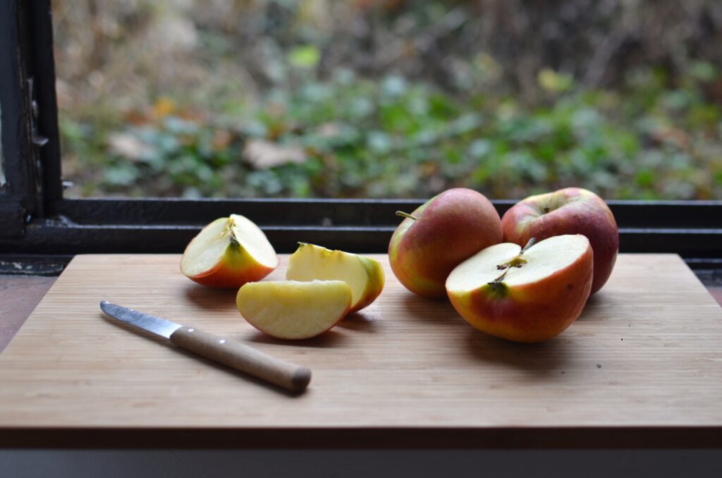 Three red apples sit on a cutting board. One of them has been sliced open with a knife.