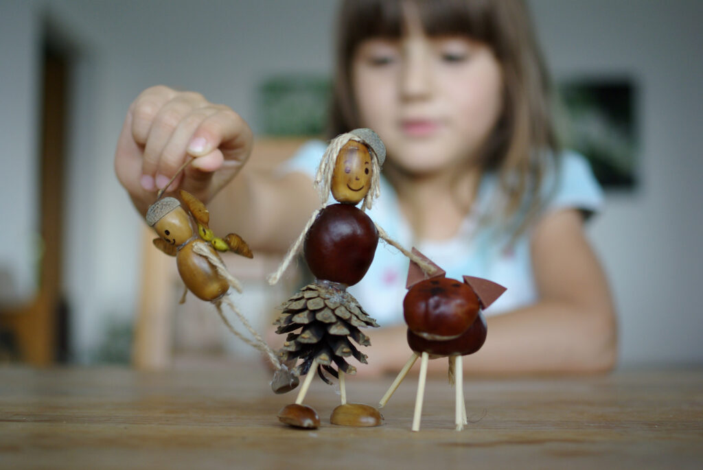 A child plays with figurines made of sticks and acorns.
