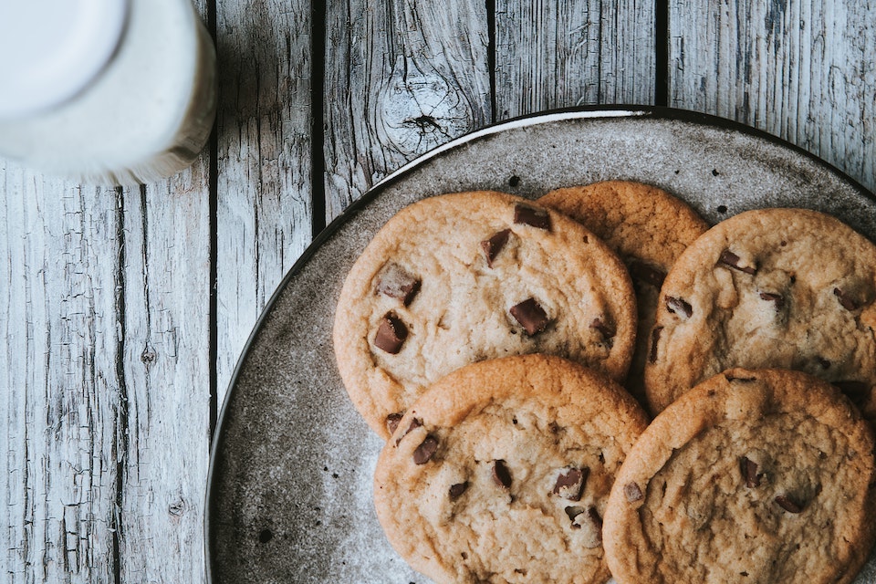 A photograph features a plate of cookies on a wooden table next to a glass of white liquid.