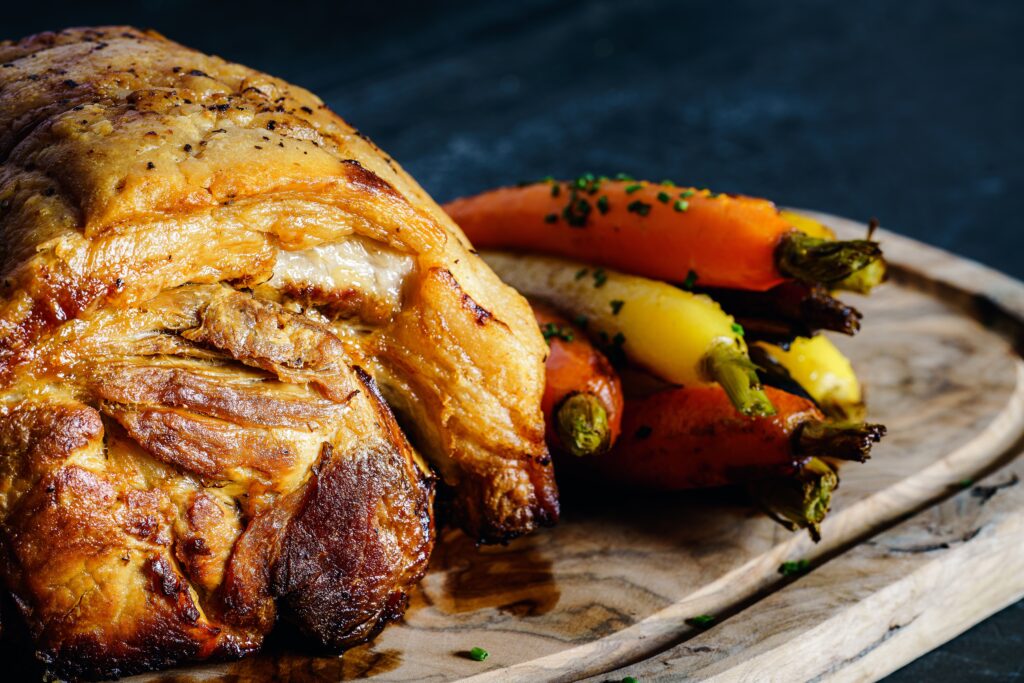 A close-up image shows a large hunk of cooked meat and orange and yellow carrots arranged on a wooden cutting board.