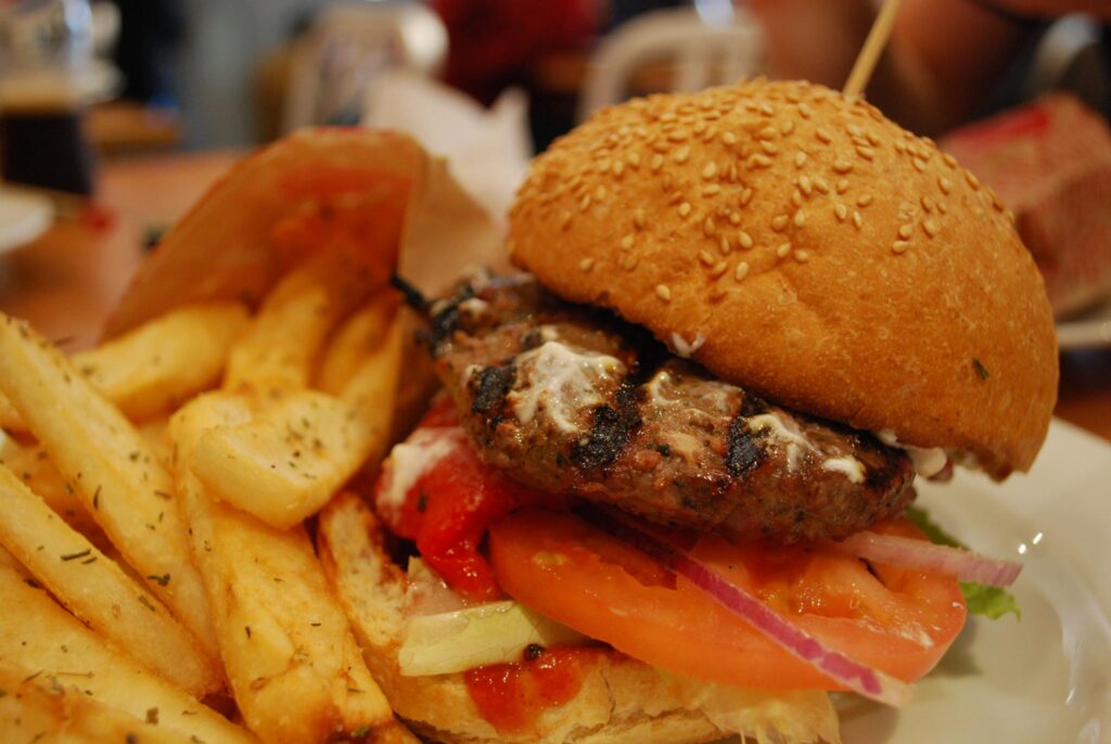 A charred burger on a bun lies next to thick cut fries on a white plate.