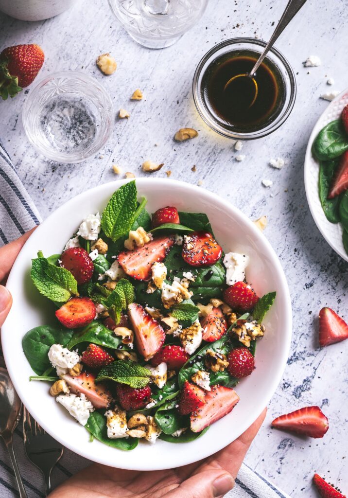 From above, a photograph features a green salad with strawberries, cheese, and nuts in it.