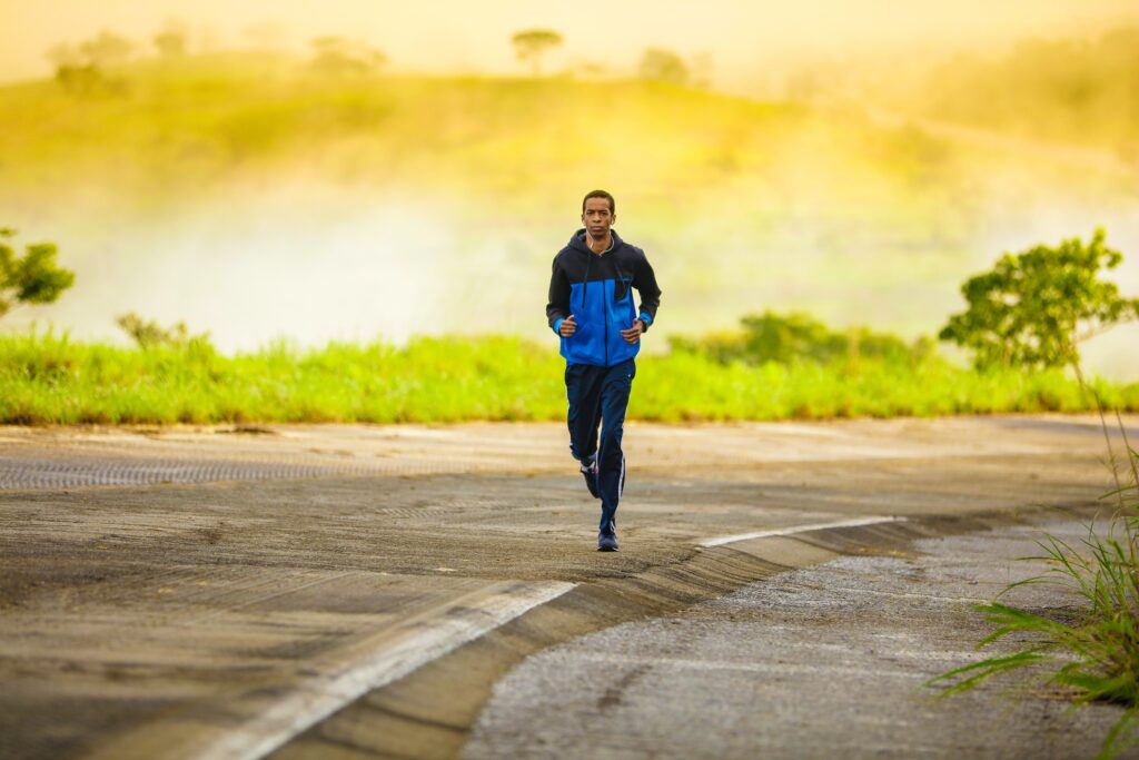 A person with short hair in athletic gear runs on the side of an asphalt road.
