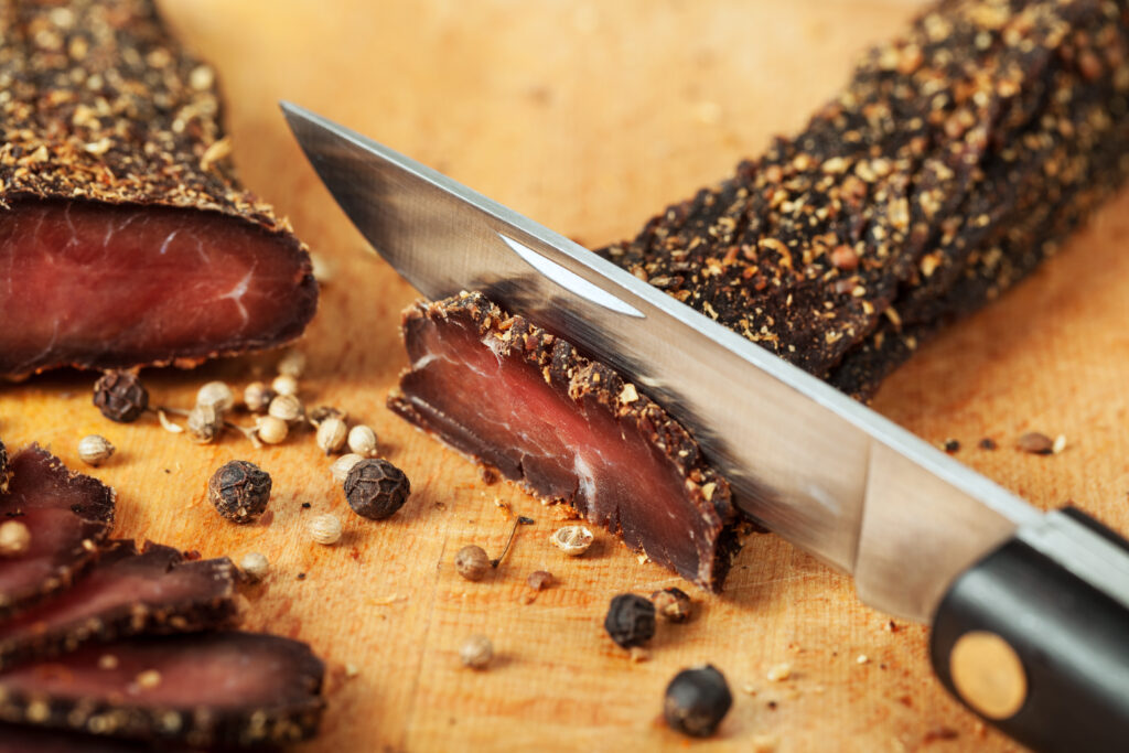 A knife cuts strips of dried, copiously seasoned meat.