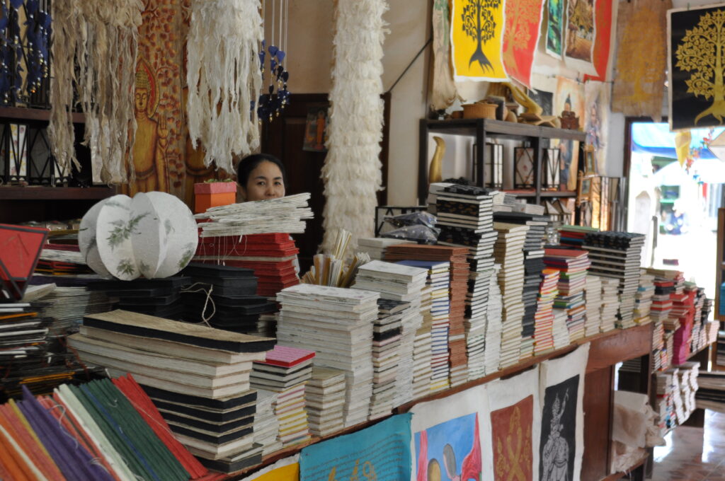 A photograph features a large counter covered with books in a crafts store. A person is barely visible behind the book piles.
