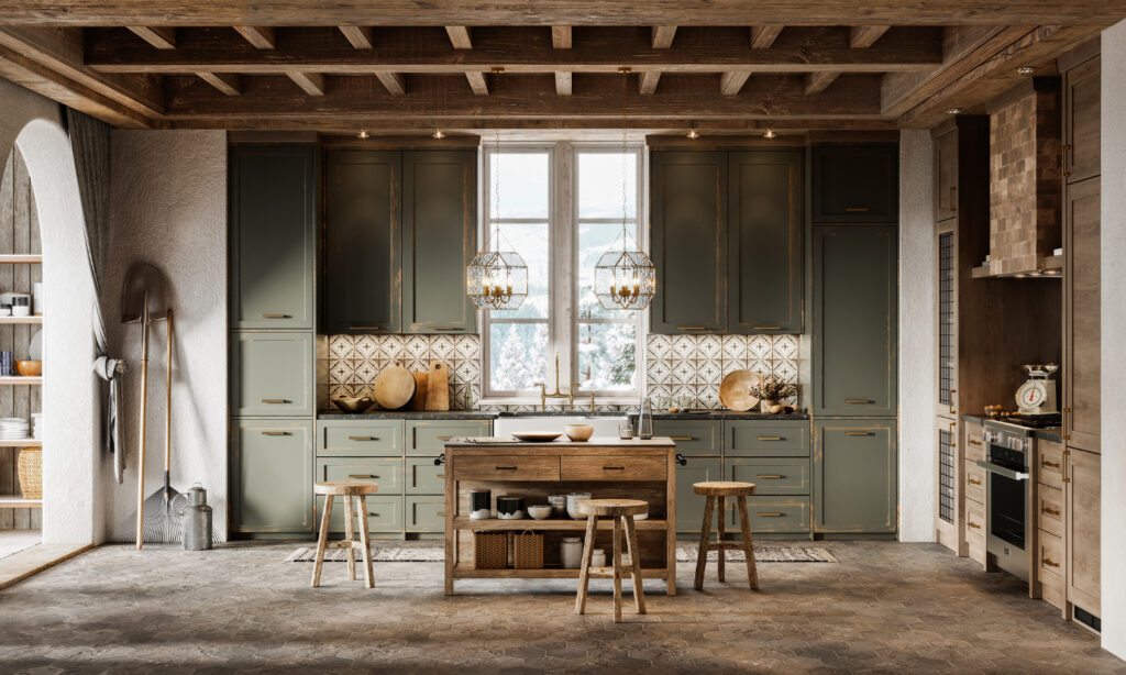 A photograph features a room with wooden ceiling beams, a small wooden island surrounded with stools, and a long kitchen counter and large olive-green cabinets covering its far wall.
