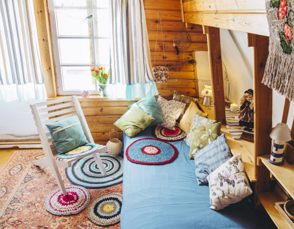 A bright blue futon and white folding chair are covered with colorful pillows and crocheted doilies.