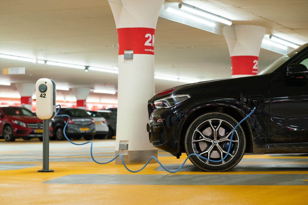 A photograph features a black car in a parking deck connected to a white machine by a cord.