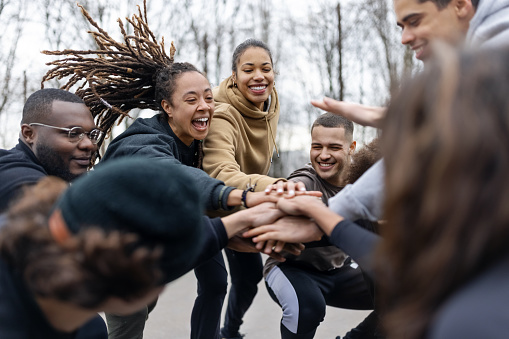 A group of smiling people is arranged in a circle with their hands extended into and stacked together in the circle’s center.