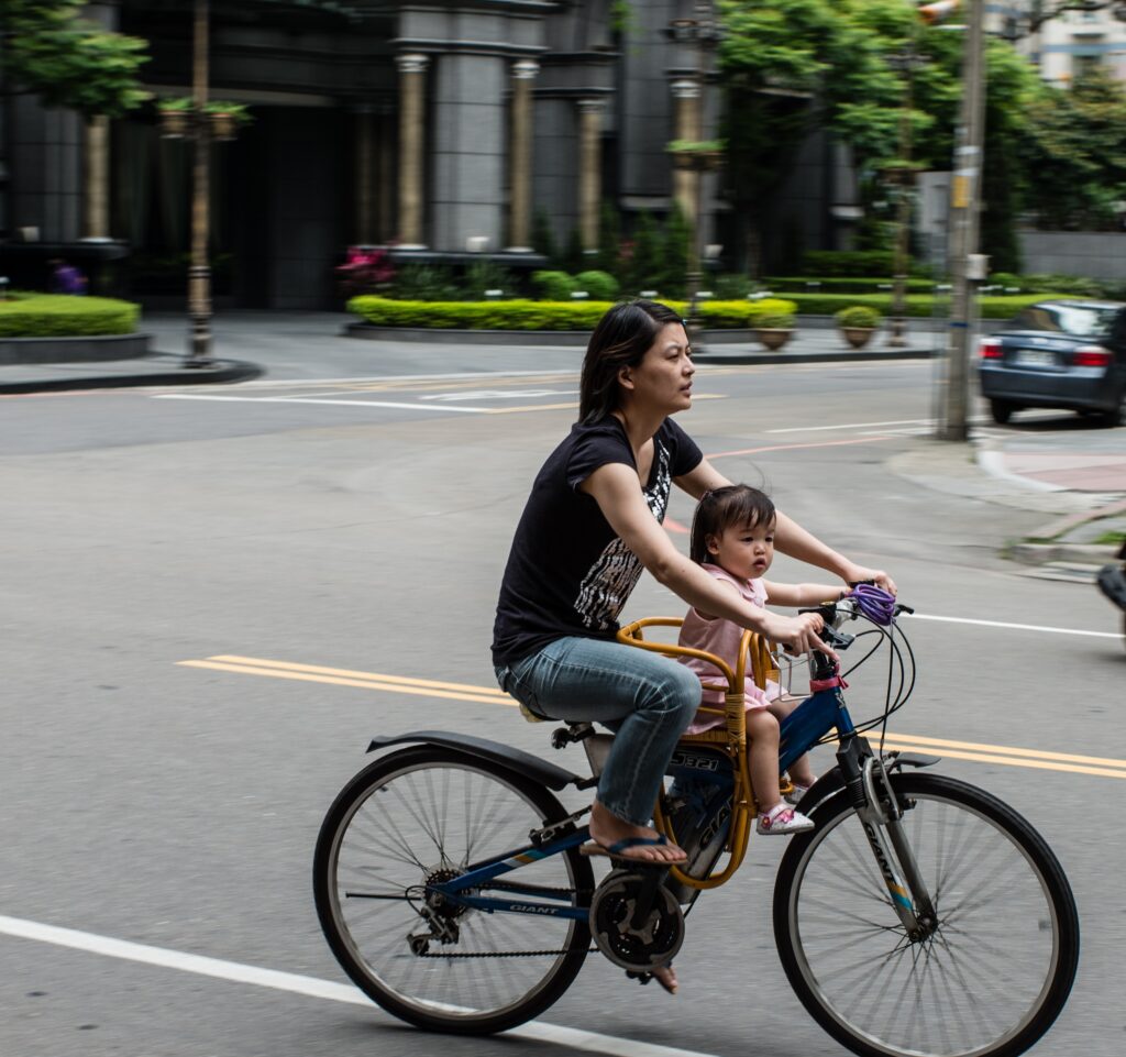 An adult with a child perched in front of her rides a bike down a road.