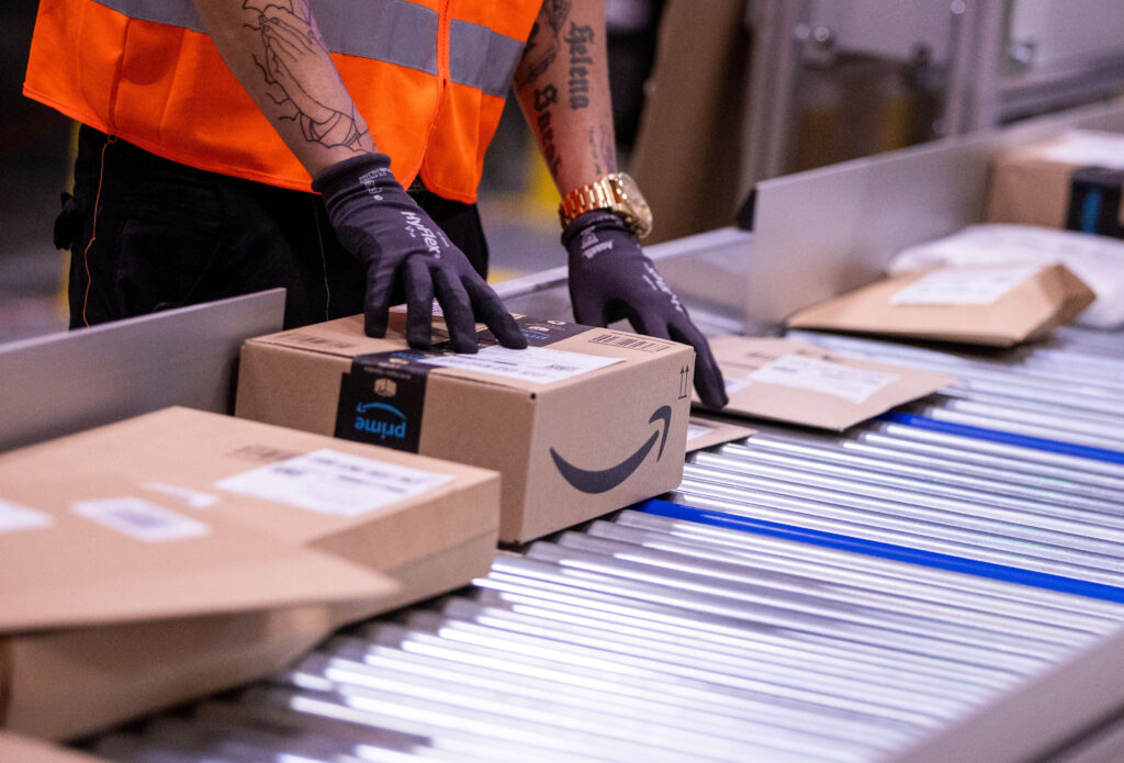 A person’s gloved hands touch an Amazon-labeled cardboard box that is one of several packages.