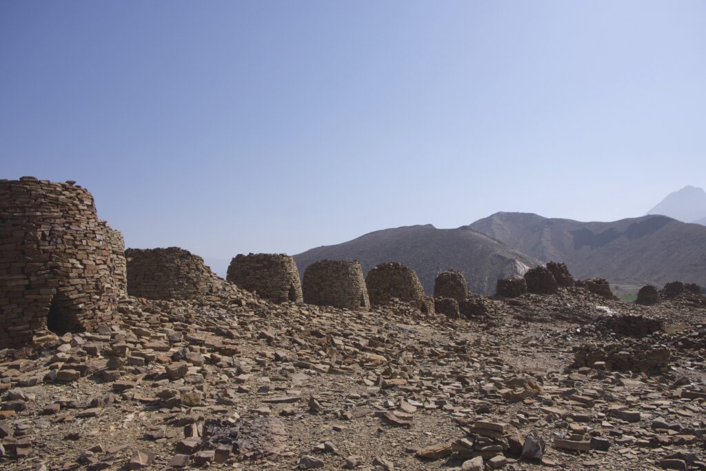 An arc of stone structures sits on rocky terrain. Mountains tower in the distance.