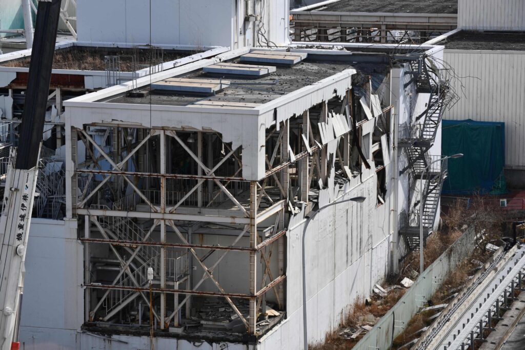 A white building’s exterior walls have been ripped off, exposing its metal skeleton and various wires.