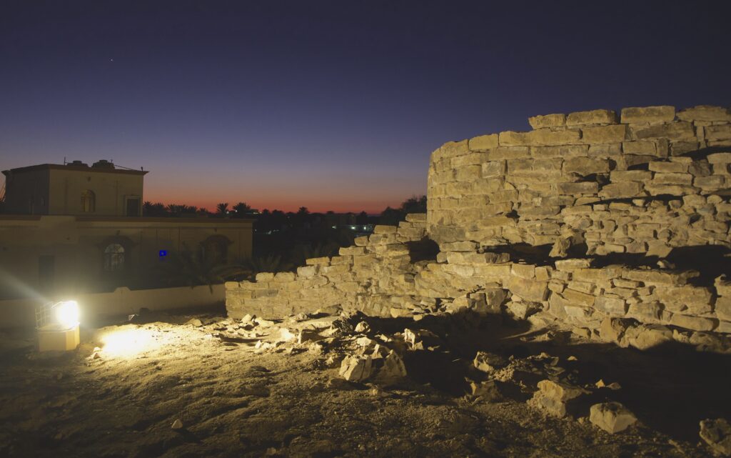 Shrouded in darkness, a round stone structure on the photo’s right side is illuminated by a light installed on the left side.