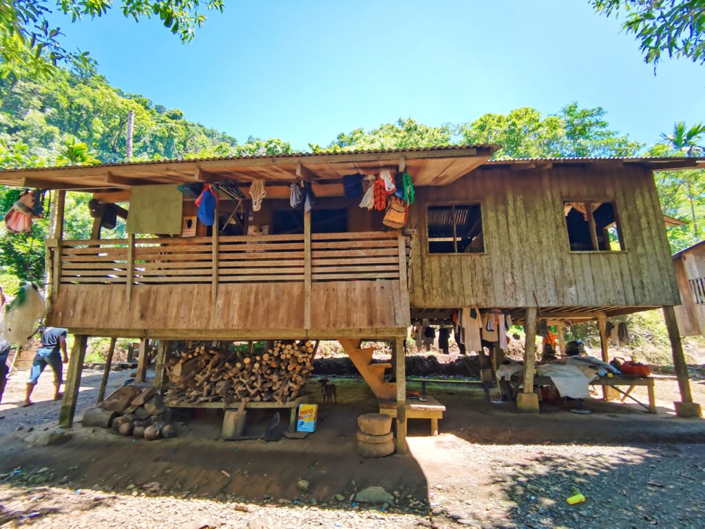 Um homem está de pé nos degraus de uma casa de madeira erguida acima do solo sobre estacas de madeira.
