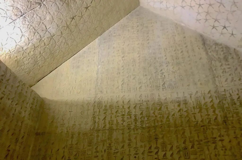 Photographed from below, a large beige stone wall and ceiling are covered in various etchings and symbols.