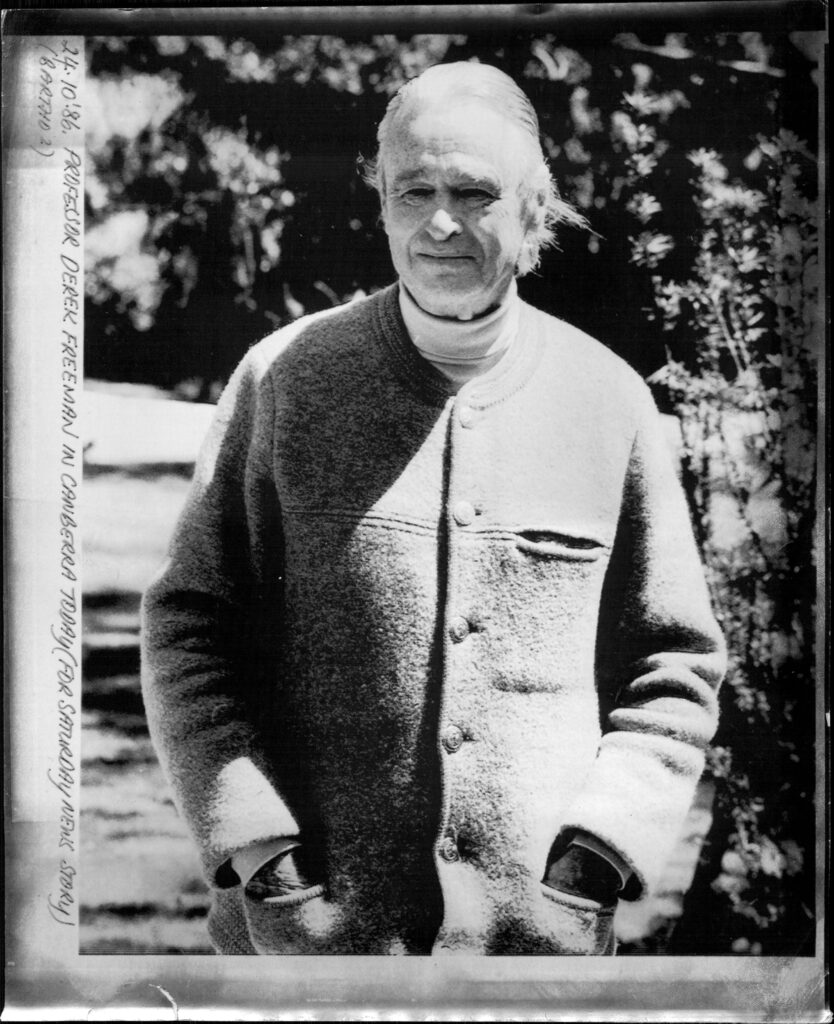 A gray-haired man stands outside with his hands in the front pockets of his buttoned-up sweater coat.