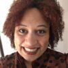 A woman with dark curly hair smiles at the camera.