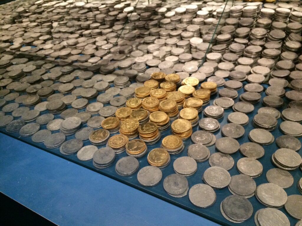 A blue table is covered with silver coins except for a square area of gold coins in the center.